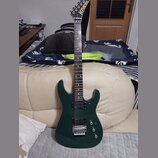 Tmavě zelená elektrická kytara s dvojsekmovým tělem a hnědým hmatníkem. Na hlavě je viditelné zlaté logo Kramer. Nástroj je vybaven dvěma humbuckery…