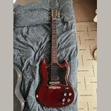 Elektrická kytara s červeně hnědým lakem a černým pickguardem. Na hlavě krku je viditelné logo Epiphone. Nástroj vykazuje mírné opotřebení povrchu v…