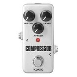 Bílý efekt pedál s nápisem COMPRESSOR a značkou KOKKO v dolní části. Pedál má tři černé ovládací knoflíky s popisky SUSTAIN, LEVEL a ATTACK. Uprostře…