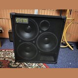 Černý basový reproduktor v kostkovém korpusu s textilním potahem a kovovou ochrannou mřížkou. V horním levém rohu je umístěno žluté logo s nápisem EP…