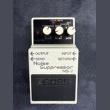 Bílý efekt pedál s černým ovládacím panelem a černým gumovým spínacím tlačítkem. Na spodní části je nápis Noise Suppressor NS-2 a logo BOSS. Horní pa…