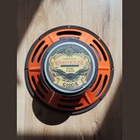 Kytarový reproduktor s oranžovým kovovým rámem a černým vnějším prstencem. Na středovém štítku je nápis WAREHOUSE GUITAR SPEAKERS, AMERICAN VINTAGE,…