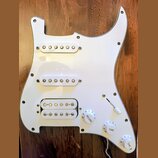 Bílá pickguard pro elektrickou kytaru s třemi snímači. Horní dva snímače jsou jednoduché (single-coil) a spodní je humbucker s dvěmi řadami pólů. Sou…