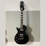 Černá elektrická kytara s tvarem singlecut a krémovým lemováním. Na hlavě je bílý nápis Bach. Nástroj má dva humbuckery, čtyři ovládací knofíky a stр…