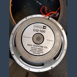 Fotografie znázorňuje zadní stranu reproduktoru v kovovém rámu. Na bílém štítku je uvedeno logo Celestion, model G12-100 a nápis Impedance 15 ohms. D…