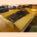 V otevřeném kartonovém krabici se nachází svazek šedých kabelů. Kabely jsou v krabici naskládané a zamotané. Na jednom z konců je viditelný kovový ko…