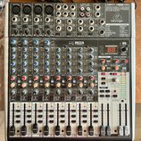 Stříbro-šedý mixážní pult s černými ovládacími prvky. V pravém horním rohu je nápis XENYX X1622USB a logo behringer. Přístroj obsahuje více vstupních…