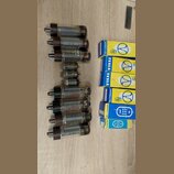 Fotografie zobrazuje skupinu elektronických vakuových elektronek a jejich originálních krabiček na dřevěném povrchu. Na některých elektronkách je čit…