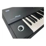 Černý klávesový nástroj s bílými a černými klávesami. Na horním panelu jsou bílé nápisy KORG a MUSIC WORKSTATION m50. V levé části je umístěn kulatý…