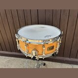 Dřevěný snare drum s přírodním povrchem a chromovaným kováním. Na blaně je viditelné logo REMO a na korpusu štítek s nápisem B.L.A. Custom Line Produ…