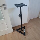 Černý kovový stojan s trojúhelníkovou základnou a plochou horní deskou. Na jedné z hran základny je bílý nápis NOWSONIC. Povrch stojanu vykazuje mírn…