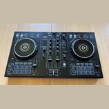 Černý DJ kontrolér s dvěma jog-koly a centrálním mixážním sekcí. Na přístroji je bílý nápis Pioneer DJ a modelové označení DDJ-400 s doplňkem rekordb…