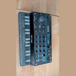 Černý hybridní syntetizátor s modrými detaily a nápisem Pro VS MINI HYBRID VECTOR SYNTHESIZER. Na levé straně je umístěno logo behringer a blok tlačí…