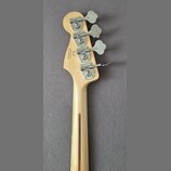 Zadní strana hlavy a krku světlé dřevěné basové kytary. Na hlavě jsou čtyři kovové ladičky a nápisy „Fender“, „Custom Offset“, „Made in USA“ a sériov…