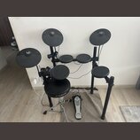 Elektronická bicí souprava v černé barvě s černým rámem. Na sedáku je bílé logo a nápis YAMAHA. Souprava obsahuje několik padů, tři činely a pedál s…