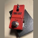 Červený efekt pedál s nápisem PHASER a značkou Rowin. Na horní straně se nachází černý ovládací knoflík s popiskem SPEED a přepínač s nápisy VINTAGE…