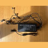 Černý napájecí adaptér s nápisem MULTI POWER SUPPLY, SEPARATE ISOLATED, 8 x 9V DC/100mA + 2 x 9V DC/300mA a STARBUCK. Z jednotky vychází deset černýc…