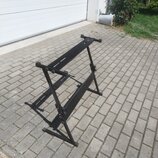 Černý kovový stojan na klávesové nástroje v rozloženém stavu. Stojan má X-tvarovou konstrukci s nastavitelnou výškou a gumovými koncovkami na nohách.…