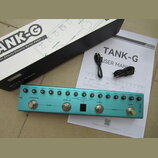 Na fotografii je modrý efektový pedál s nápisem M-VAVE a označením TANK-G. Zařízení má čtyři stupadla s popisky A/REVERB, B/DELAY, C/MOD a D/AMP, řad…
