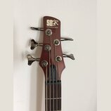 Fotografie zachycuje hlavu hnedý basové kytary s четыřmi ladicími kolíky. Na horní části je bílý nápis „SOUNDGEAR“ v stylizovaném logu a pod ním menš…