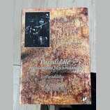 Fotografie znázorňuje obal knihy nebo sešitu s texturou připomínající rezavý kov. V levém horním rohu je černobílá fotografie bubeníka za bicími nást…