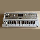 Bílá klávesová syntezátor s nápisem KORG microKORG synthesizer vocoder. Přístroj má v horní části ovládací panel s několika otočnými knoflíky, tlačít…