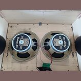 Dva reproduktory značky CELESTION s nápisy LOUDSPEAKERS, G12 a Vintage 30. Reproduktory mají béžové rámy a jsou umístěny v dřevěné bedně. Mezi nimi j…