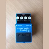 Modrý efekt pedál s nápisy Compression Sustainer a CS-3. Na horní části jsou čtyři bílé ovládací knoflíky s popisky LEVEL, TONE, ATTACK a SUSTAIN, če…