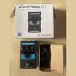 Fotografie zobrazuje efekt pedál VoiceTone C1 značky TC HELICON v původním kartonu s přibaleným napájecím adaptérem. Na zařízení je vidět nápis TC HE…