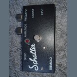 Černý efekt pedál s nápisem Schaller a TREMOLO. Na horní hraně jsou dva ovládací knoflíky s popisky AMPLITUDE a FREQUENZ, dále nápisy OUTPUT a INPUT.…