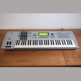 Stříbrný digitální klavír s klávesnicí. Na levé straně je logo YAMAHA a vpravo nápis MOTIF ES6. Nástroj má centrální displej, několik posuvníků a sad…