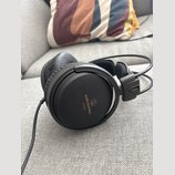 Černá velká sluchátka s uzavřeným provedením a koženým polstrováním náušníků. Na vnější straně náušníku je nápis audio-technica a modelové označení A…