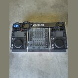 Sada DJ equipmentu v transportním kufru. Uprostřed je černý mixážní pult s nápisy ALLEN&HEATH a xone, po stranách jsou dva identické černé přehrávače…