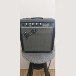 Černý kytarový kombozesilovač s šedou textilní maskou reproduktoru. Na předním panelu je nápis Frontman 10G a pod ním FENDER MUSICAL INSTRUMENTS, na…