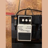 Bílý efekt pedál značky BOSS s nápisem Noise Suppressor NS-2. Zařízení má tři ovládací knoflíky s popisky REDUCTION, THRESHOLD a DECAY, přepínač MODE…