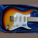 Elektrická kytara s trupem v barevném přechodu od žluté přes oranžovou k červené a černé. Nástroj má bílý pickguard, tři jednoduché snímače a tři ovl…