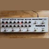 Stříbrný efektový procesor s nápisy T-REX a MAGNUS by TREX ENGINEERING Denmark. Zařízení obsahuje pět sekcí s ovládacími knoflíky a přepínači, označe…