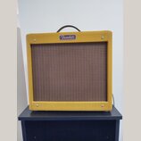 Žlutý kytarový kombozesilovač s hnědou textilní maskou reproduktoru. V horní části je umístěno bílé logo s nápisem Fender. Nástroj má černou přenosno…