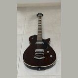 Tmavně hnědá elektrická kytara s polodupovým tělem a bílým lemováním. Na černém plechtraci je viditelné logo GRETSCH a nápis Broadkaster. Nástroj má…