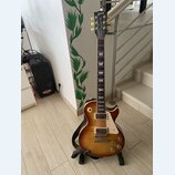 Elektrická kytara s trupem ve tvaru Les Paul v barvě sunburst. Na hlavě je nápis Gibson a pod ním slovo Traditional. Nástroj má dva humbuckery, čtyři…