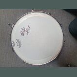 Bílá bubenová koženka s kovovým obručem. Na povrchu je v levé části černý nápis REMO a logo REMO s doplňujícím textem AMBASSADOR COATED WHITE. V horn…