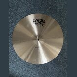Kruhový mosazný činel s broušeným povrchem. Na povrchu je černý nápis „EXTRA THIN 18"“ a logo „Paiste Masters“. Činely vykazují mírné zaprášení.