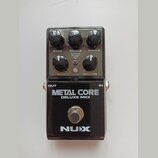 Černý kytarový efekt s nápisy METAL CORE a DELUXE MKII. V horní části jsou pět kontrolních knoflíků s popisky BASS, MIDDLE, TREBLE, GAIN a MASTER, př…