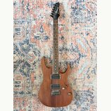 Elektrická kytara s hnědým dřevěným povrchem těla a hnedou hmatníkem. Na hlavě je bílý nápis Ibanez. Nástroj má dva humbuckery, jeden ovládací knoflí…