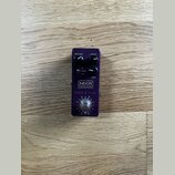 Fialová efekt pedál s kovovým tělem. Na horní části jsou tři černé ovládací knoflíky s popisky VOLUME, DRIVE a TONE a přepínač s nápisy BOOST a DIST.…
