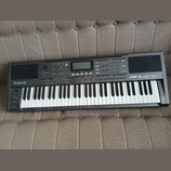 Černý digitální klavír s bílými a černými klávesami. Na levé straně je bílý nápis Roland a vpravo nápis EXR-5s INTERACTIVE ARRANGER. Horní panel obsa…