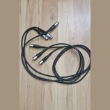 Na fotografii jsou dva černé audio kabely s konektory typu XLR. Kabely mají černou barvu a jsou svinuty do smyček na dřevěné podlaze. Na konektorech…