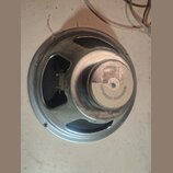 Fotografie znázorňuje zadní stranu reproduktoru s kovovým rámem a magnetem. Na bílém štítku magnetu je nápis PROFESSIONAL LOUDSPEAKER a označení G12.…