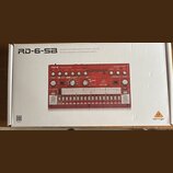 Fotografie znázorňuje krabici s červeným analogovým bicím automatem. Na krabici je nápis RD-6-SB Analog Drum Machine with 8 Drum Sounds, 64 Step Sequ…