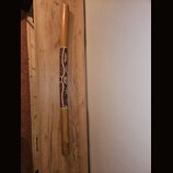 Dřevěný didgeridoo v přirozené hnědé barvě. Střed nástroje je zdobený ornamentálním vzorem v červených, bílých a žlutých odstínech. Na nástroji nejso…